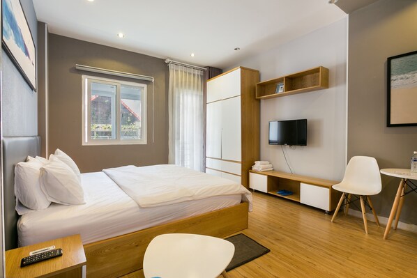 Una habitación de hotel moderna con una cama grande, un escritorio, una silla, un televisor y una ventana con cortinas.