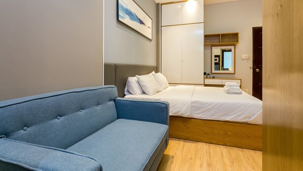 Een moderne hotelkamer met een blauwe bank, een bed met witte lakens, een houten vloer en een grote spiegel aan de muur.