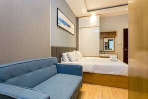 Een moderne hotelkamer met een blauwe bank, een bed met witte lakens, een houten vloer en een grote spiegel aan de muur.