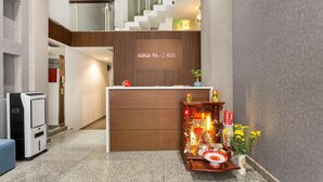 Een hotel receptie met een houten balie, een trap en een klein altaar met offers.
