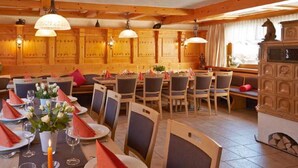 Un restaurant aux murs lambrés, avec de nombreuses tables recouvertes de serviettes rouges et un grand buffet orné de sculptures décoratives.