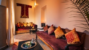 A cozy living room with a red sofa, patterned cushions, a small table with a tray of drinks, and a decorative wall hanging. - Riad Darhani (Marrakech)