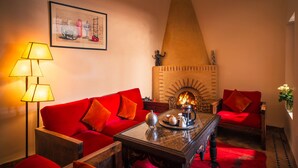 A cozy living room with a red sofa, a coffee table with a decorative item, a fireplace, and a framed picture on the wall. - Riad Darhani (Marrakech)