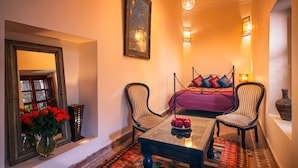 A cozy room with a bed, two chairs, a table, a mirror, and a vase of red flowers. - Riad Darhani (Marrakech)