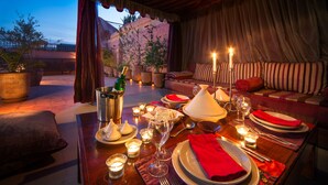 An outdoor dining area with a table set for two, featuring a bottle of champagne, a tagine, and candles. - Riad Darhani (Marrakech)