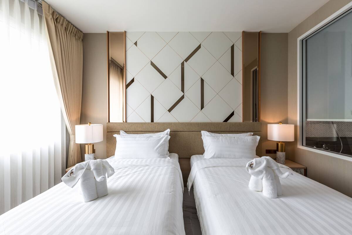 Een hotelkamer met twee bedden, een groot raam en een geometrisch wandontwerp.