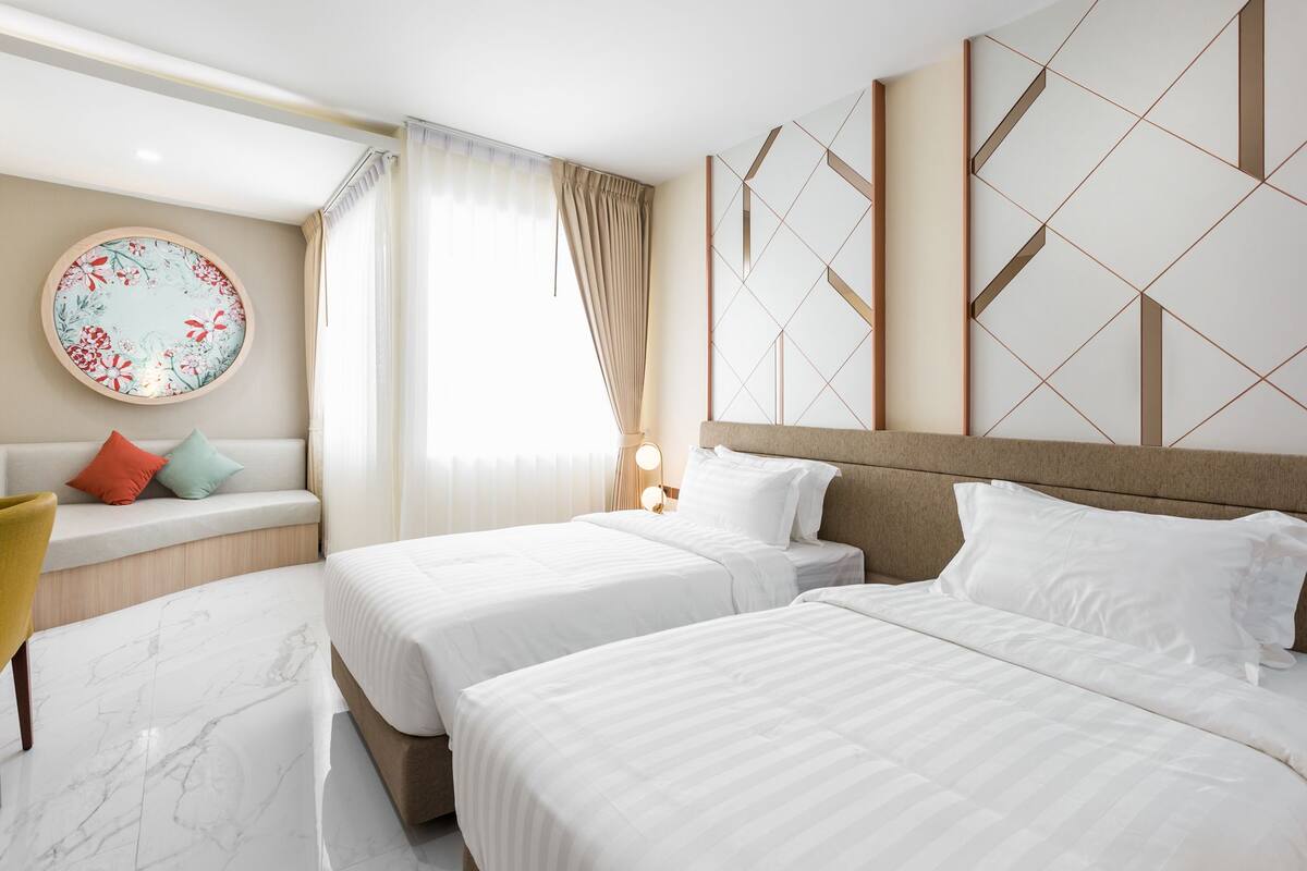 Een hotelkamer met twee bedden, een ronde wanddecoratie, een bank met kussens en een raam met gordijnen.