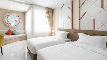 Une chambre d’hôtel avec deux lits, un élément de décoration circulaire au mur, un canapé avec des coussins et une fenêtre avec des rideaux.