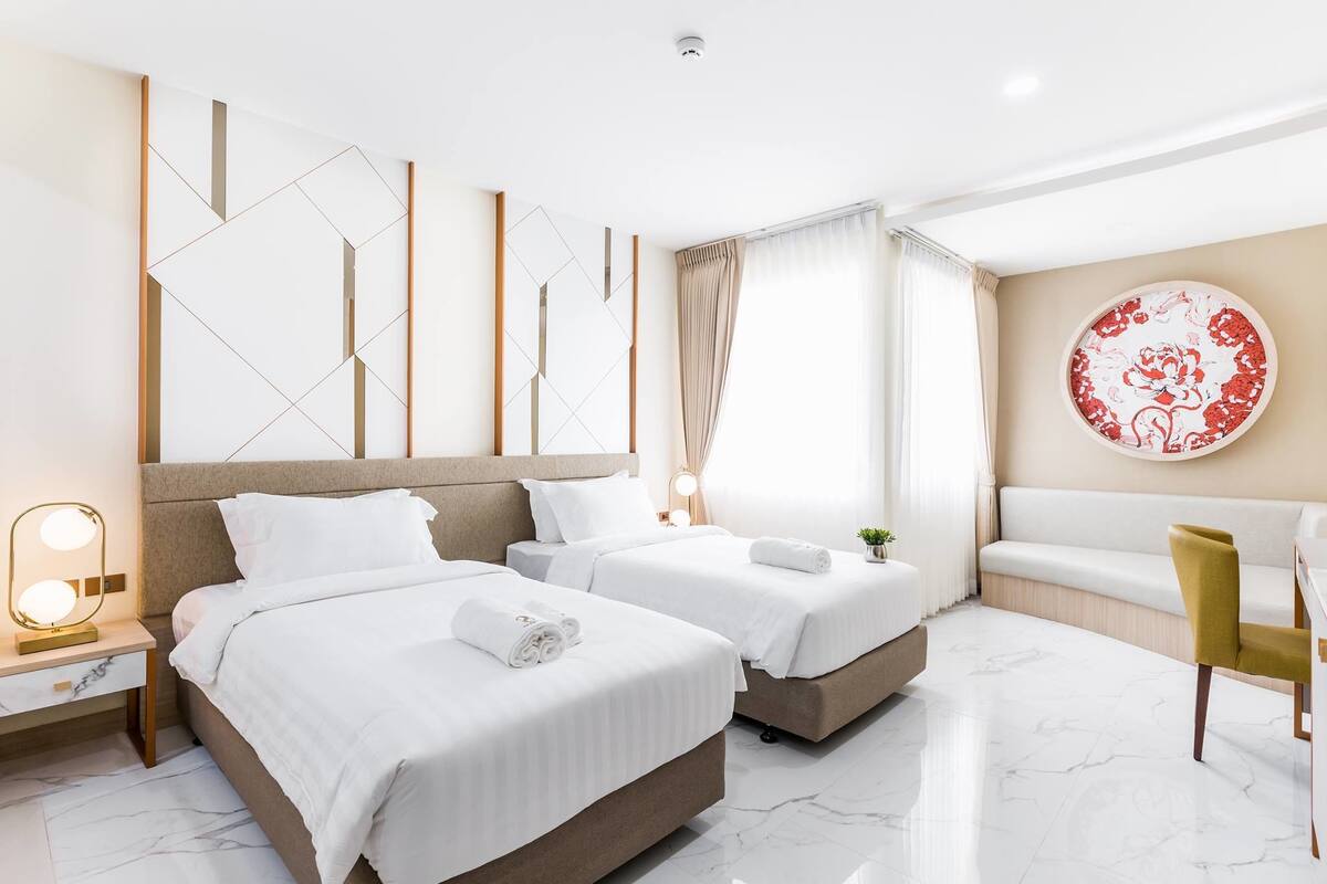 Een hotelkamer met twee bedden, een bank, een stoel, een decoratieve wand en een ronde tafel met een rood-wit patroon.