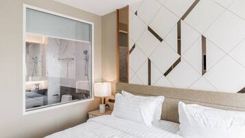 A hotel room with a large bed, a nightstand with a lamp, a window, and a geometric wall design.