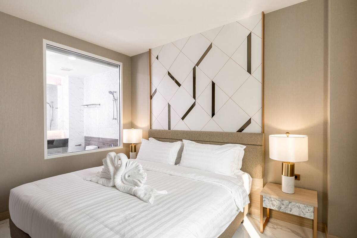 Hotelkamer met een groot bed, twee nachtkastjes met lampen, een geometrisch wandontwerp en een raam met uitzicht op de badkamer.