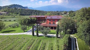 A large building with a red roof, surrounded by a well-maintained garden and vineyard. - BORGO ROMANTICO GREEN RELAIS (Cavaion Veronese)