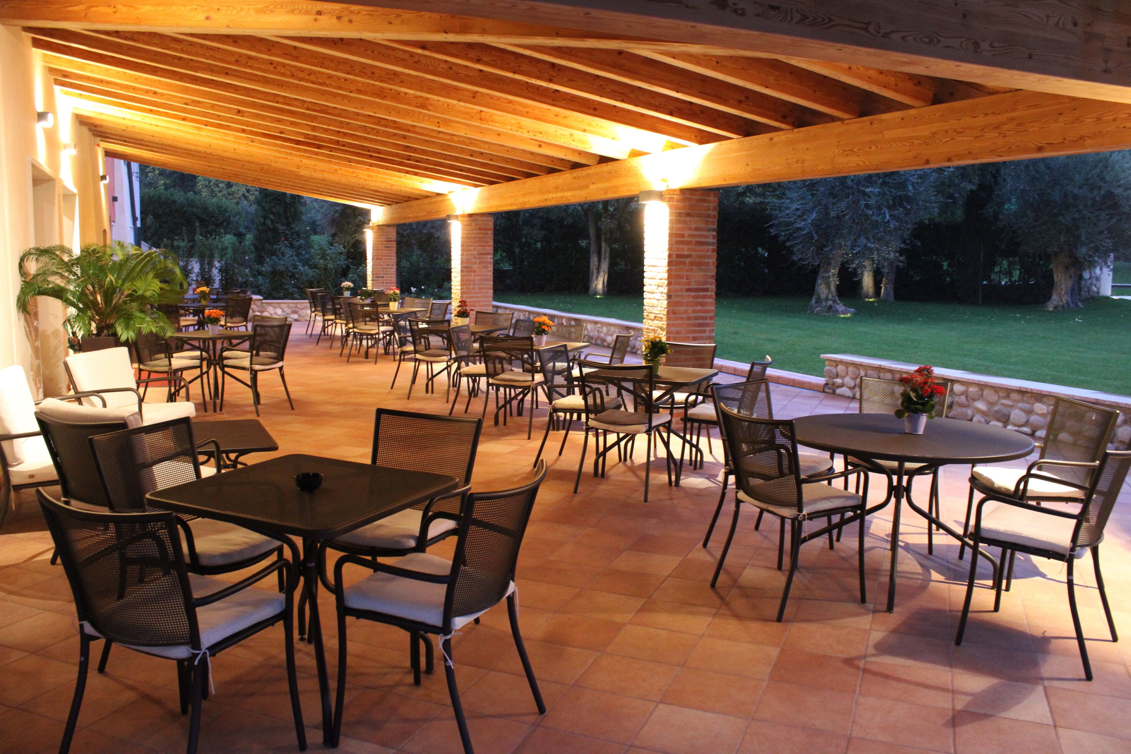 Un patio exterior con varias mesas y sillas, rodeado de pilares de ladrillo y vigas de madera.