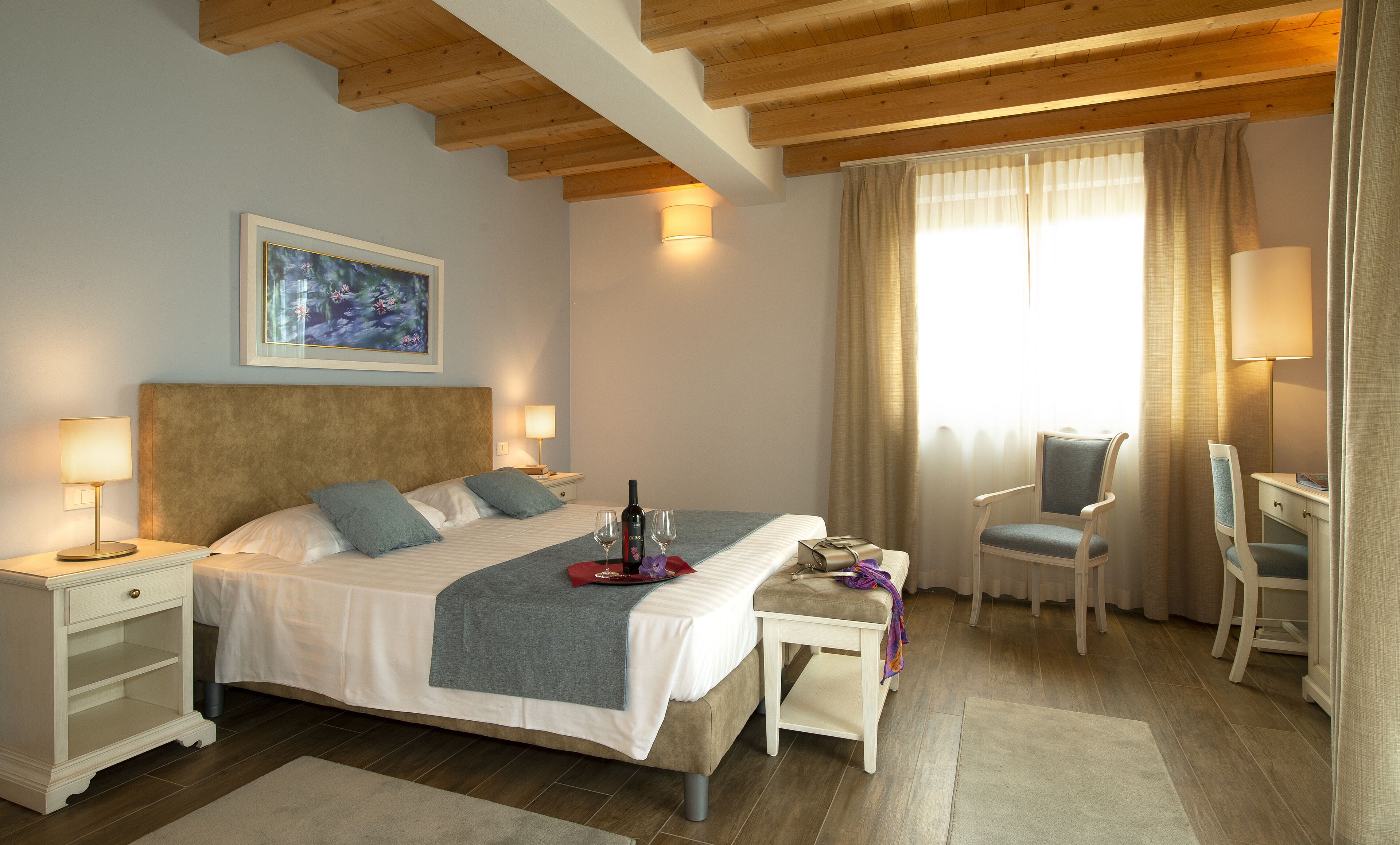 Una habitación de hotel con cama, dos mesitas de noche, un escritorio, una silla y una ventana con cortinas.
