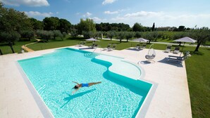 A swimming pool with a person swimming, surrounded by a grassy area with trees and lounge chairs. - BORGO ROMANTICO GREEN RELAIS (Cavaion Veronese)