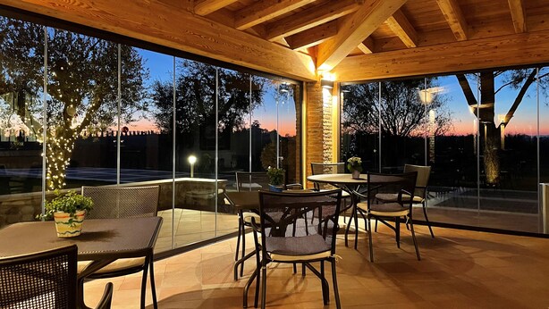 An outdoor patio area with wooden beams, glass walls, and a sunset view. - BORGO ROMANTICO GREEN RELAIS (Cavaion Veronese)