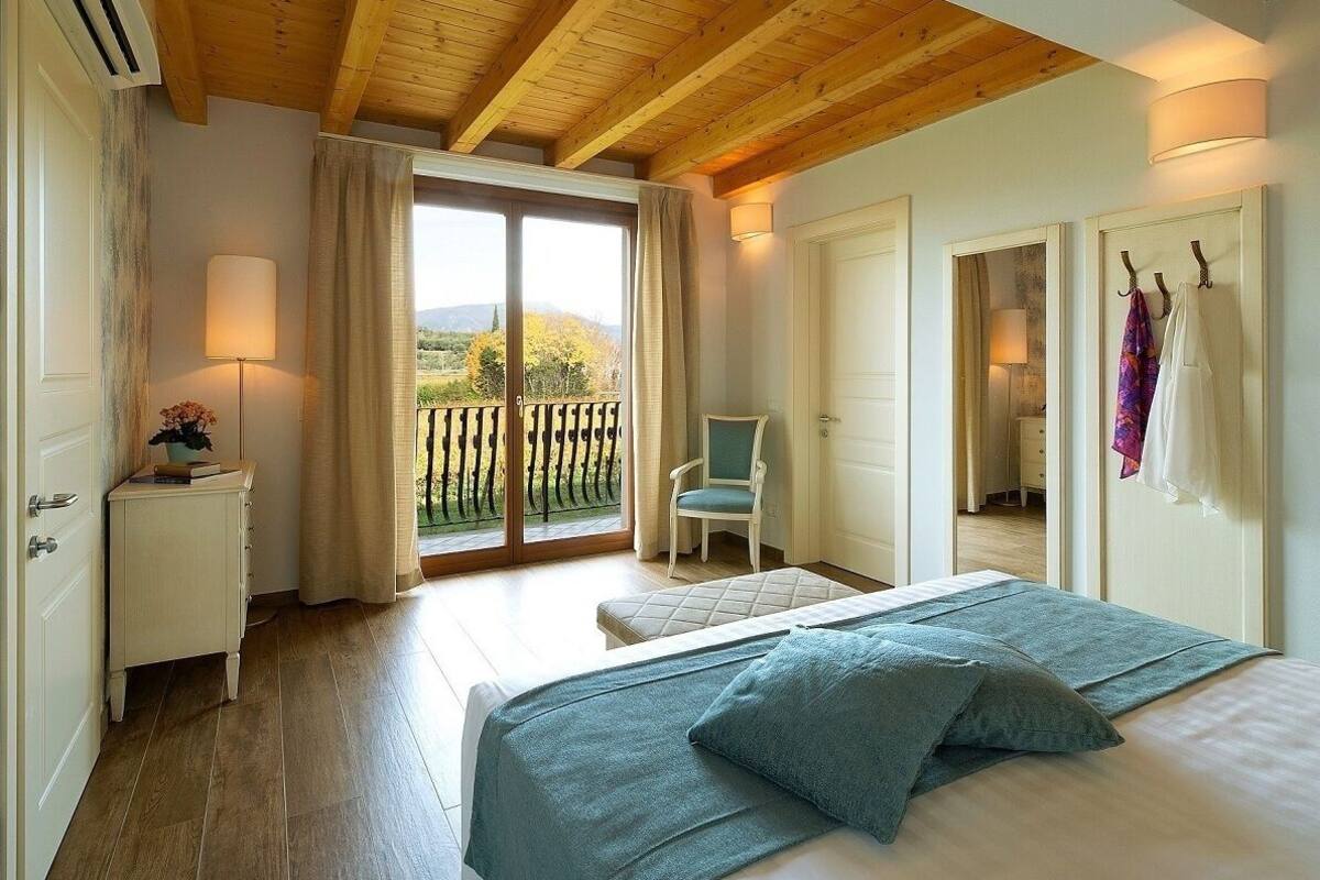 A bedroom with a large bed, a chair, a nightstand, and a view of the outdoors through a sliding door.