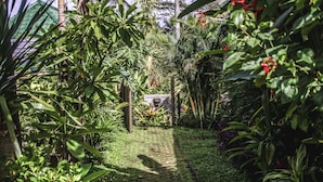 A garden pathway surrounded by lush greenery and a stone structure. - Kubu Jamu Ubud (Ubud)