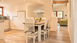 A modern kitchen with white cabinetry, a wooden dining table, and chairs. - Dauscher Hof (Siegsdorf)