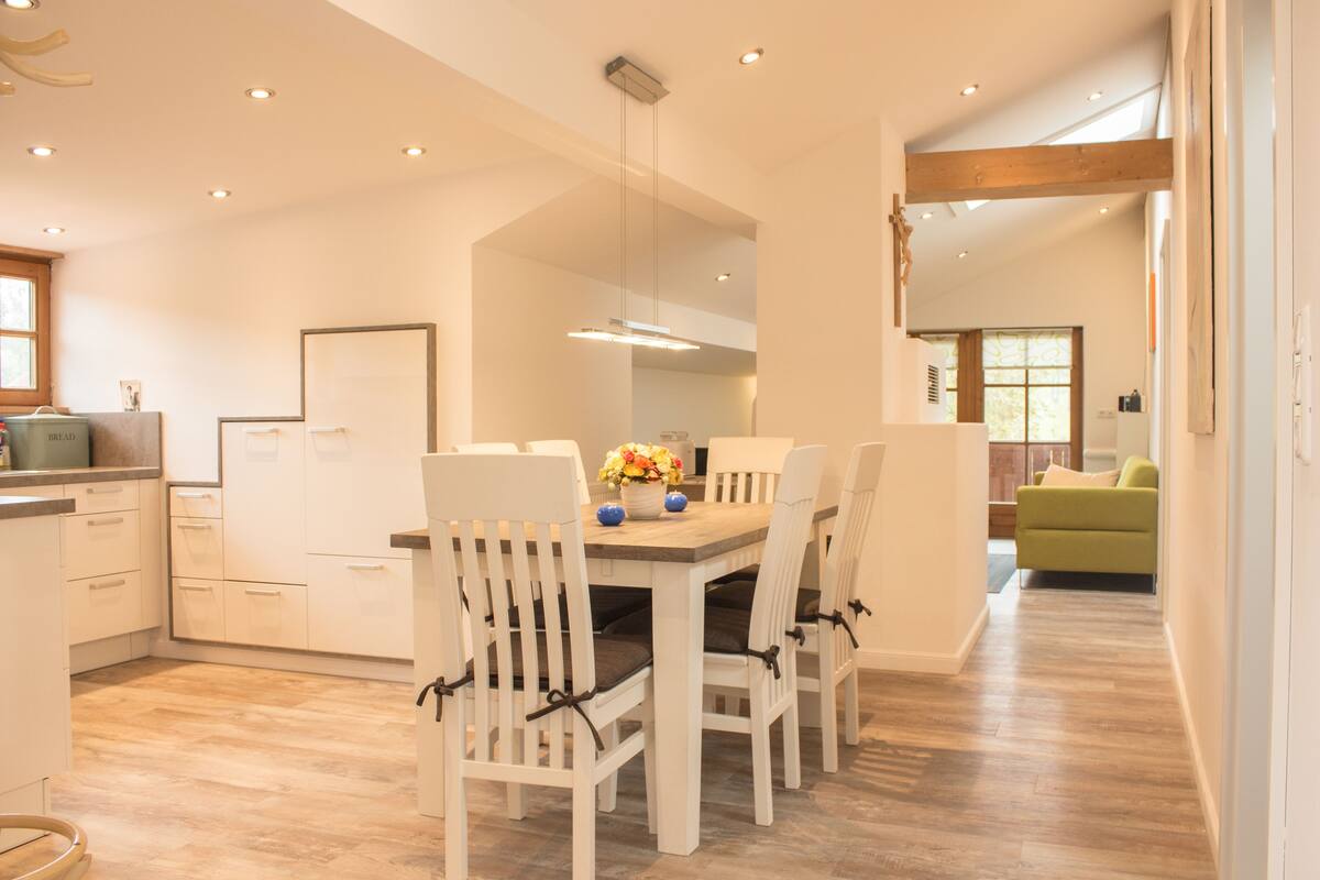 A modern kitchen with white cabinetry, a wooden dining table, and chairs.
