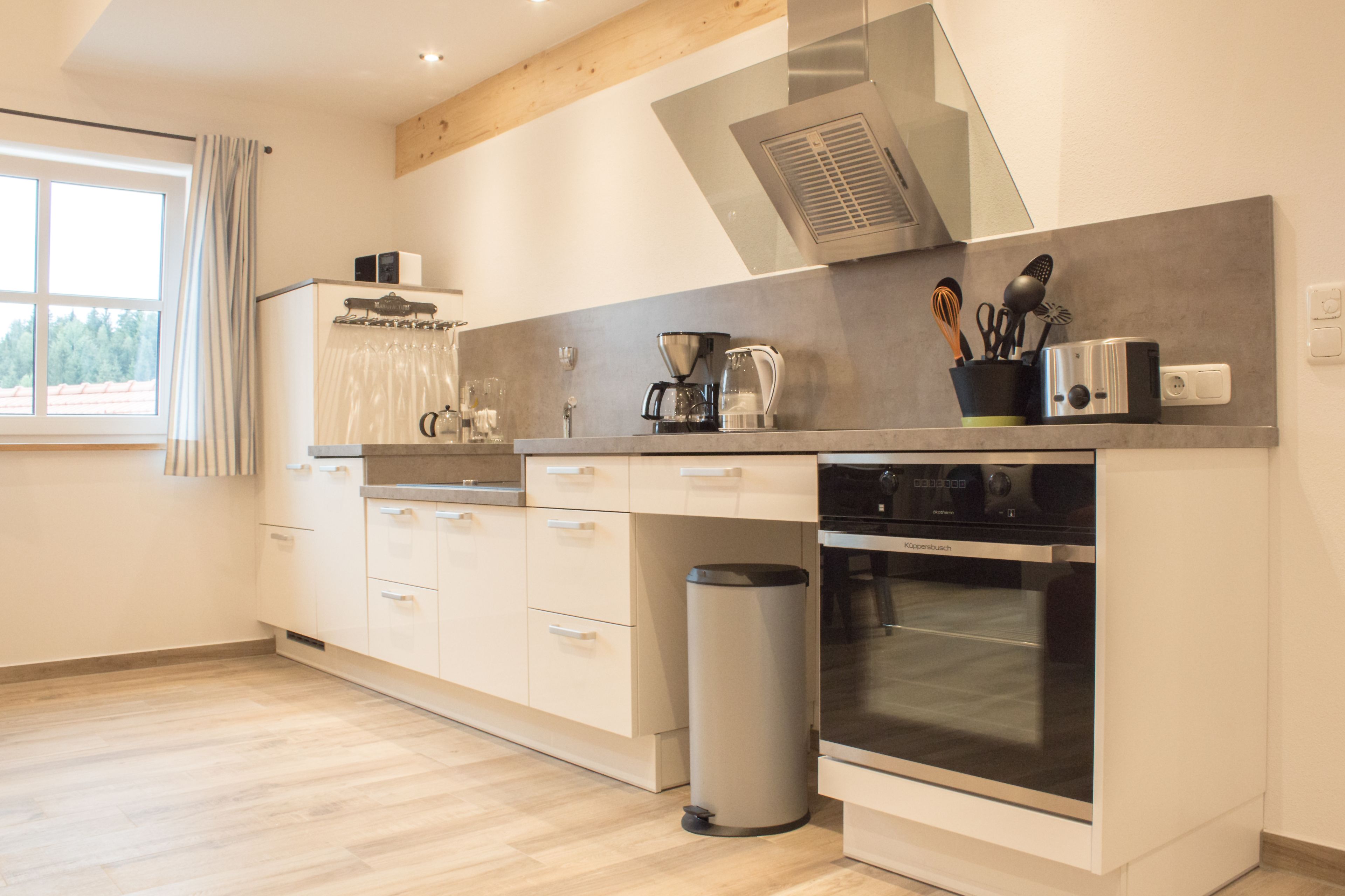 A modern kitchen with a built-in oven, a coffee maker, and a trash can.