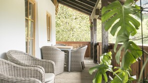 A covered outdoor seating area with wicker furniture and a table, overlooking a wooden deck and greenery. - Dauscher Hof (Siegsdorf)