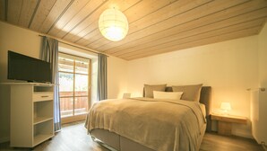 A bedroom with a bed, a TV on a stand, a bedside table with a lamp, and a window with curtains. - Dauscher Hof (Siegsdorf)