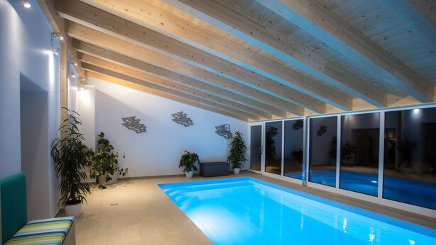An indoor swimming pool with wooden beams, potted plants, and a bench along the wall. - Dauscher Hof (Siegsdorf)