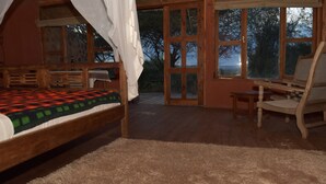 Une chambre à coucher comprenant un lit, une chaise, une table et donnant sur l’extérieur grâce à de grandes fenêtres.
