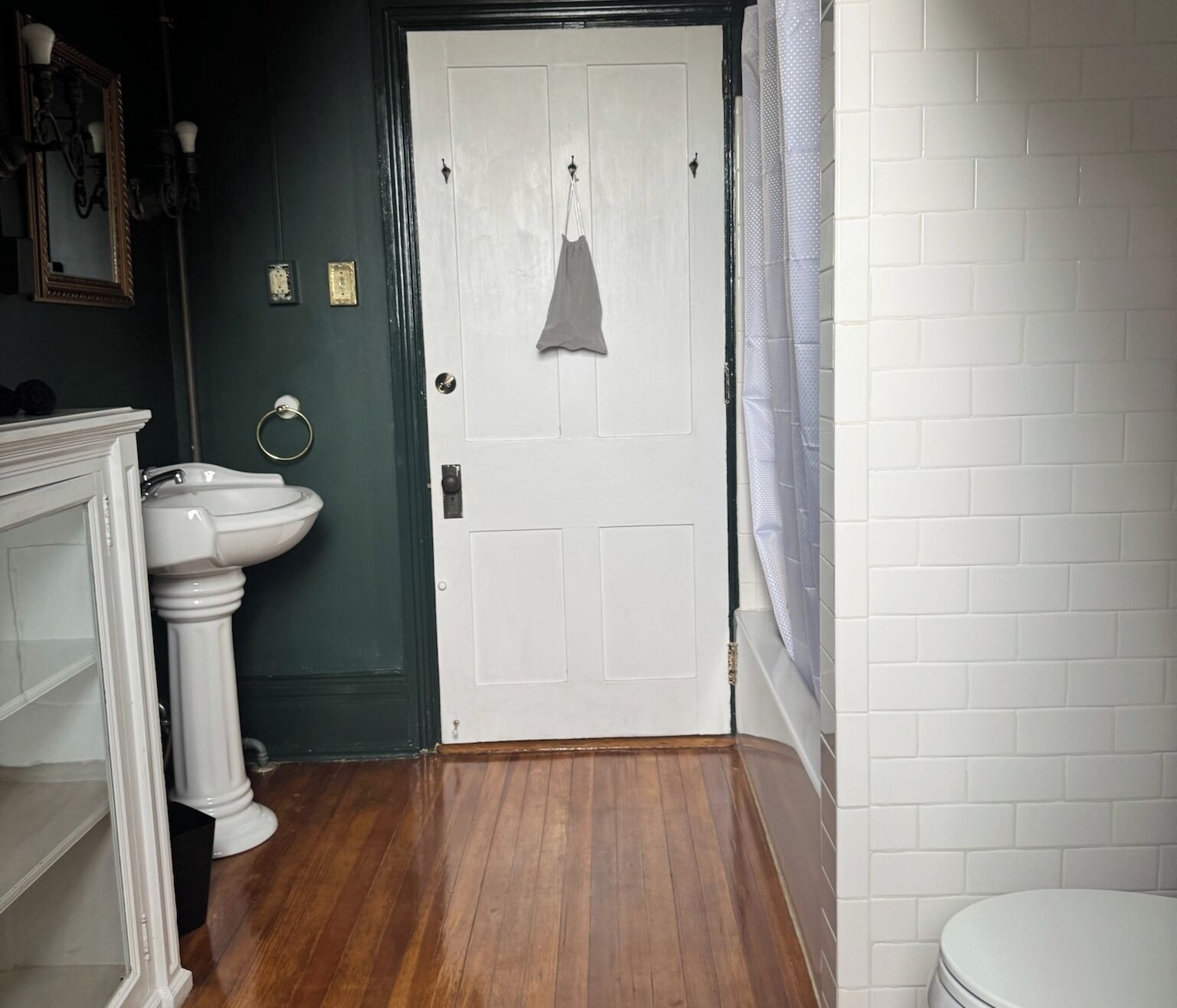 Ein Badezimmer mit einem weißen Waschbecken, einer Tür mit einem aufgehängten Handtuch und einer weißen Toilette.
