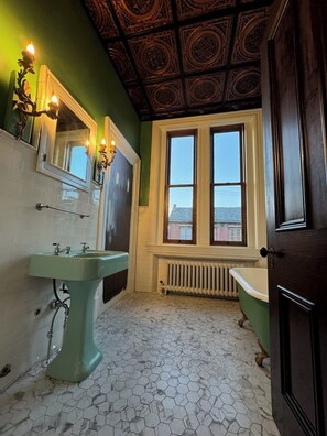 A bathroom with a green sink, a mirror, a window, and a bathtub.