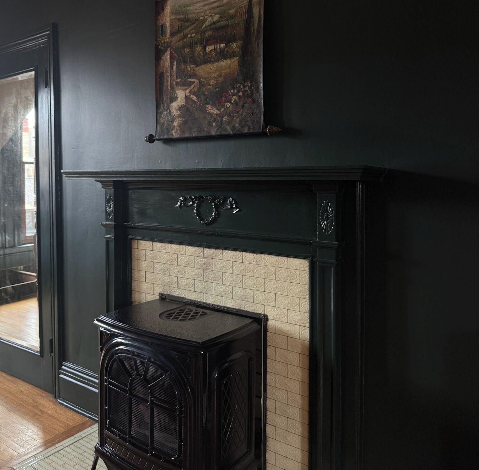 Una habitación oscura con chimenea, un cuadro encima y una estufa antigua al frente.