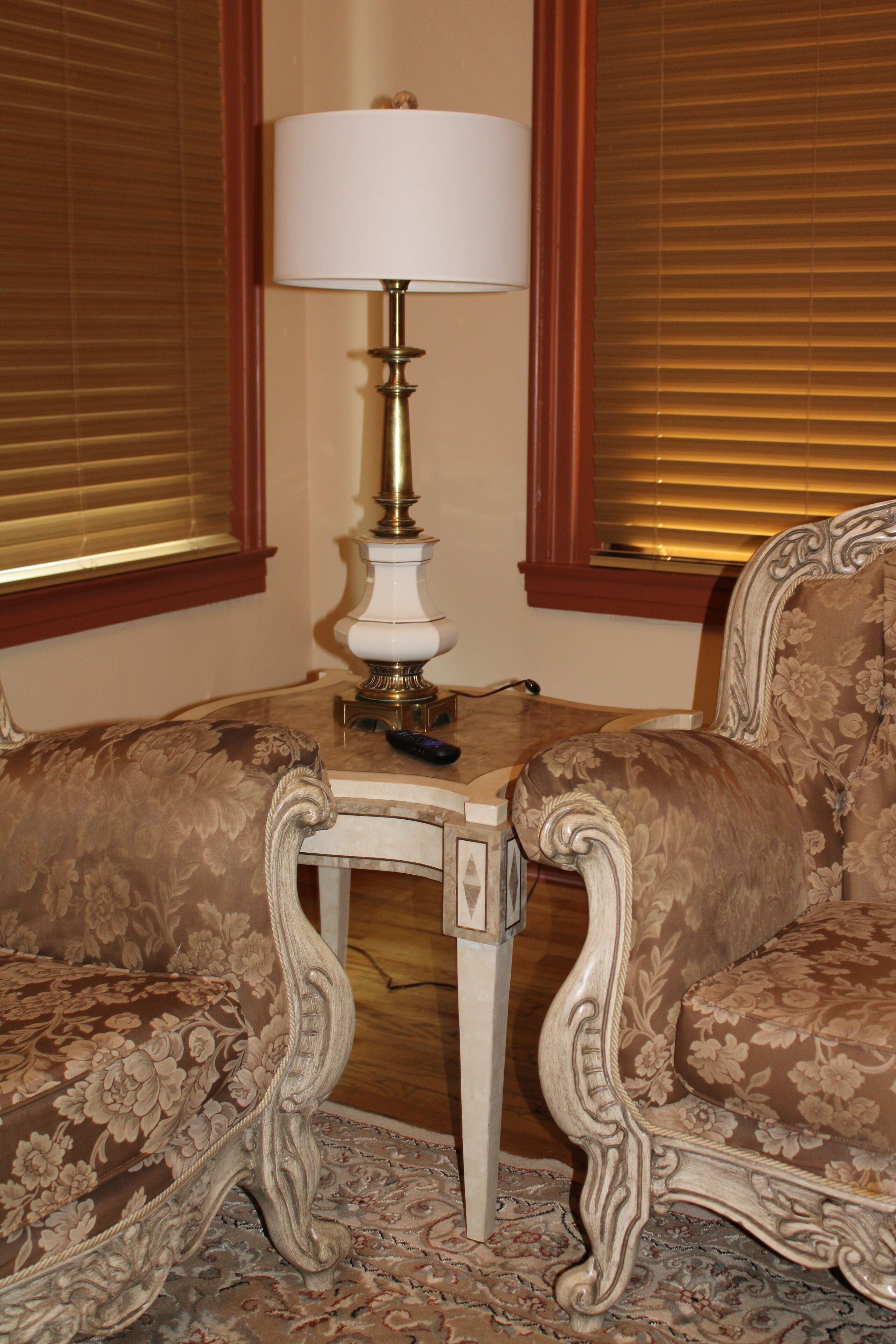 A corner room with two ornate chairs, a table with a lamp, and a patterned rug.