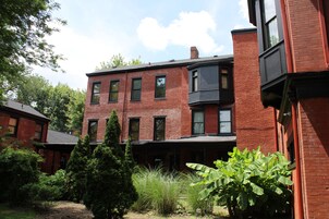 A multi-story brick building with a central courtyard, surrounded by trees and shrubs.