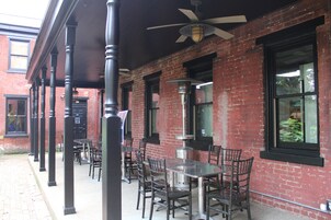 An outdoor seating area with tables and chairs, a brick building, and a ceiling fan.