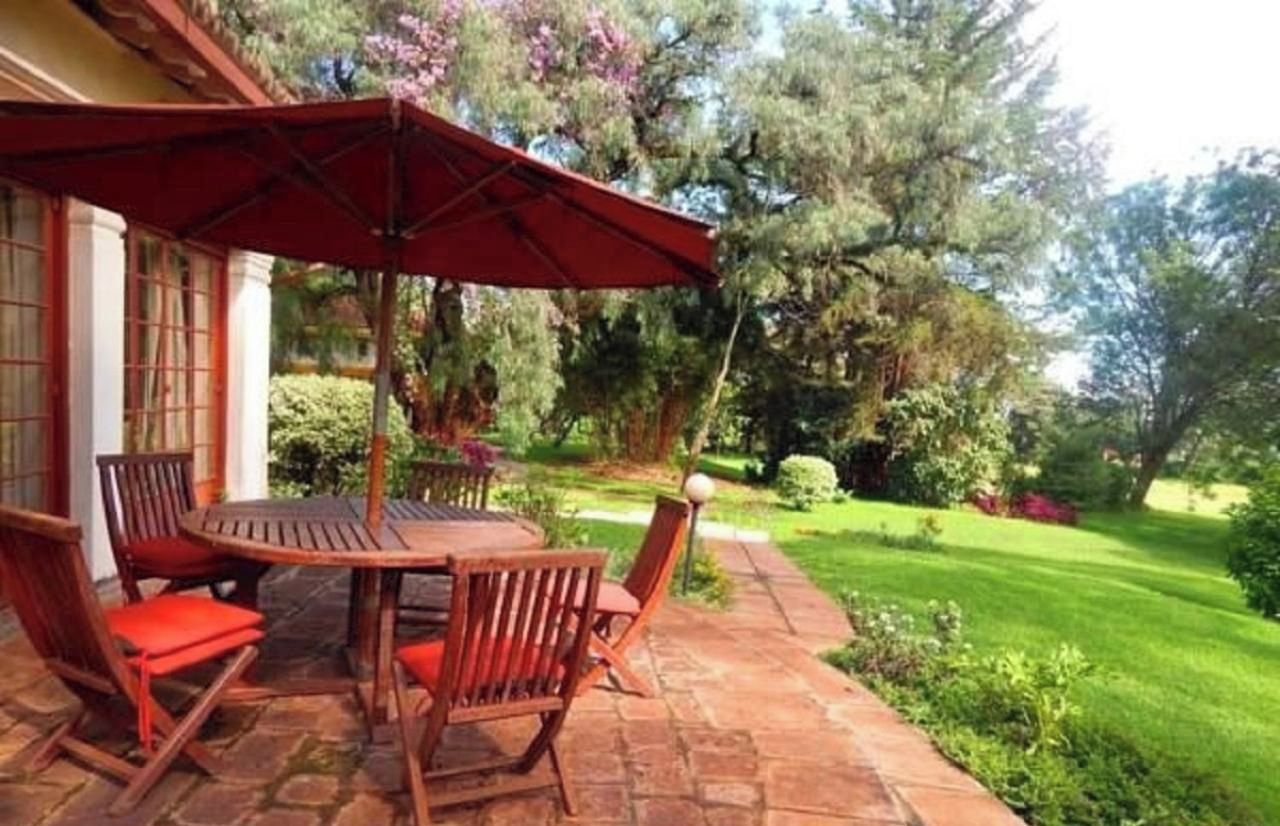 Un patio exterior con mesa y sillas, rodeado de un jardín con árboles y arbustos.