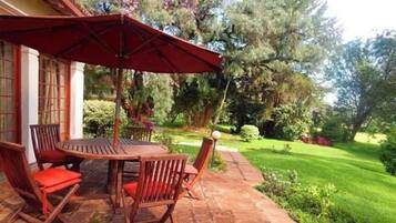 Un patio exterior con mesa y sillas, rodeado de un jardín con árboles y arbustos.