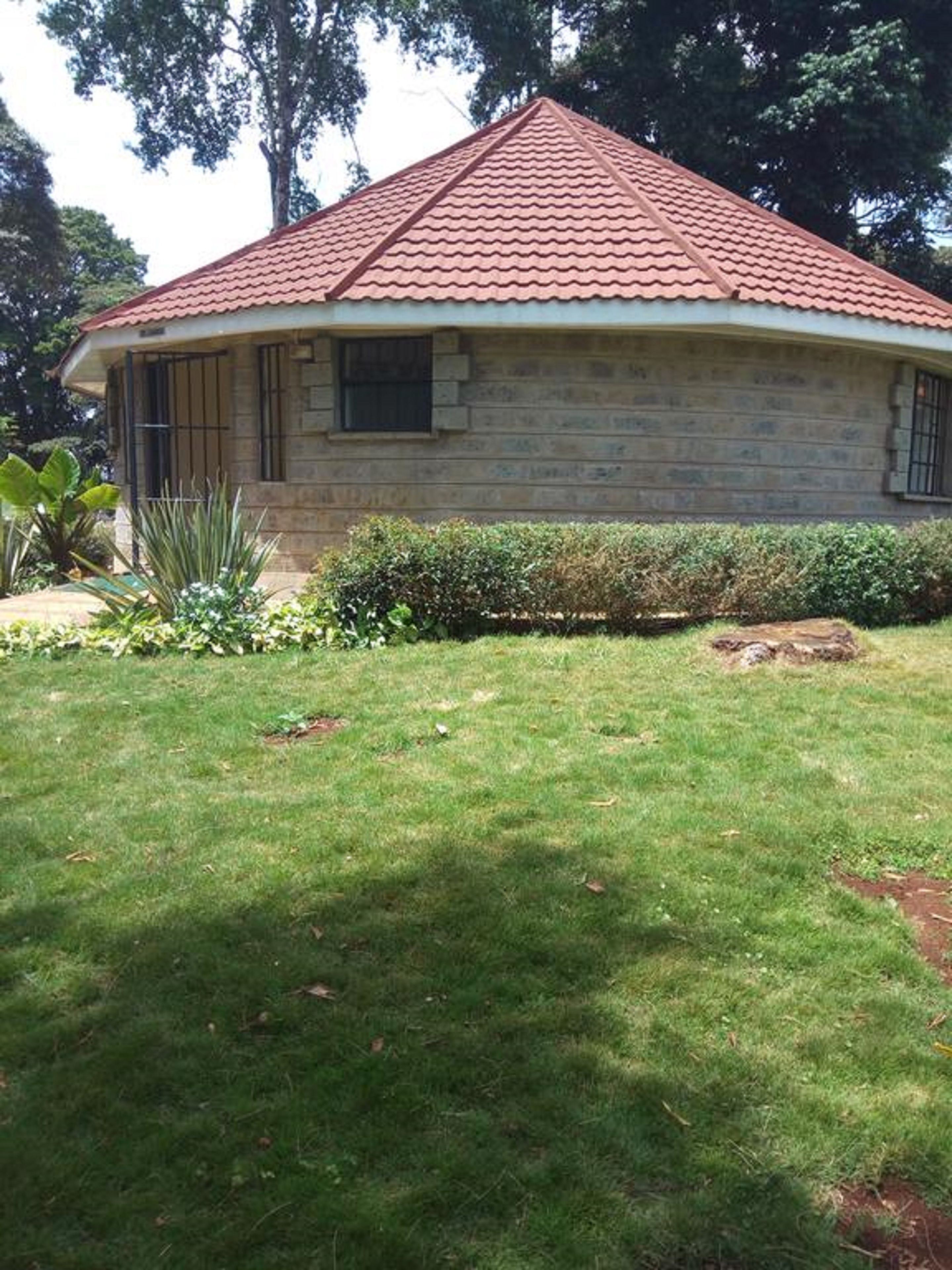 A single-story house with a red-tiled roof, a stone facade, and a small front yard with a lawn and some plants.