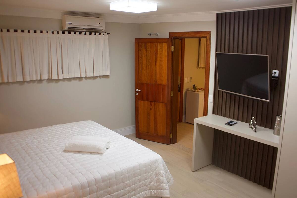 Quarto de hotel com cama, televisão, secretária e guarda-roupa.