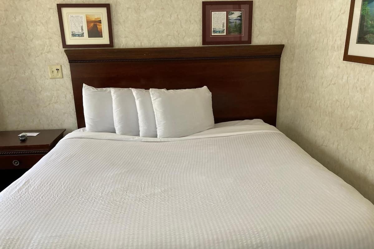 Una cama bien hecha con sábanas blancas y un cabecero de madera. Dos placas informativas enmarcadas están colgadas en la pared sobre la cama.