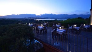 An outdoor dining area with tables and chairs, overlooking a scenic view of mountains and a body of water. - Le San Lorenzo  (Porto-Vecchio)