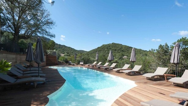 A pool area with lounge chairs and umbrellas, surrounded by a wooden deck and greenery. - Le San Lorenzo  (Porto-Vecchio)