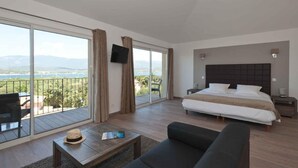 A bedroom with a large bed, a sofa, a small table, and a TV. There is a balcony with a view of the mountains. - Le San Lorenzo  (Porto-Vecchio)