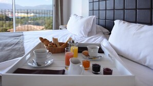 A neatly made breakfast tray with croissants, juice, and coffee on a bed with a city view. - Le San Lorenzo  (Porto-Vecchio)