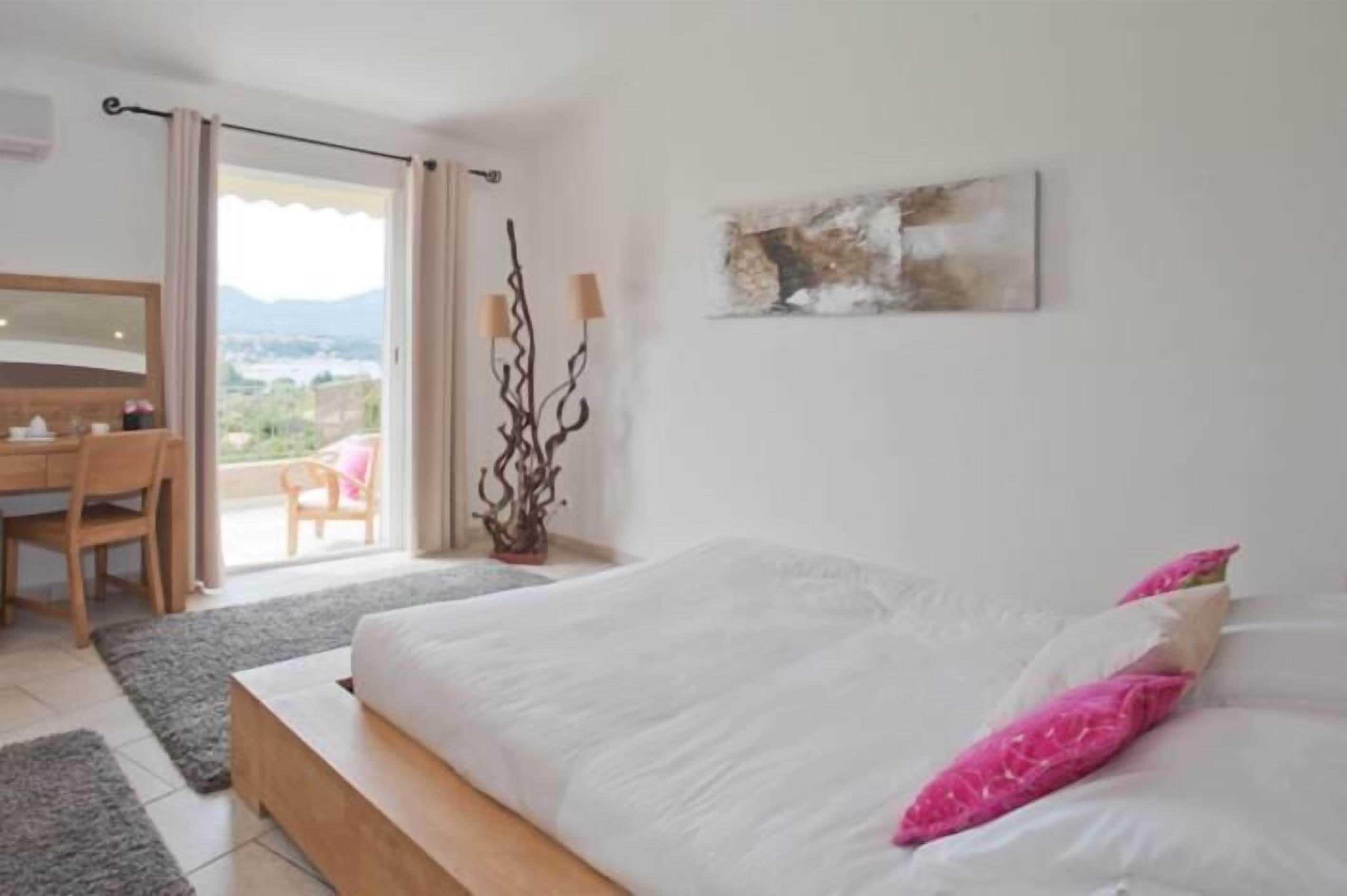 A bedroom with a bed, a desk, and a chair. There is a view of the outdoors through a sliding door.