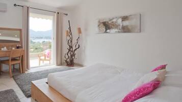 A bedroom with a bed, a desk, and a chair. There is a view of the outdoors through a sliding door.