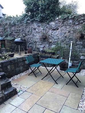A patio with a stone wall, a barbecue grill, and green folding chairs. - Clontarf Seafront Luxury (Dublin 3)