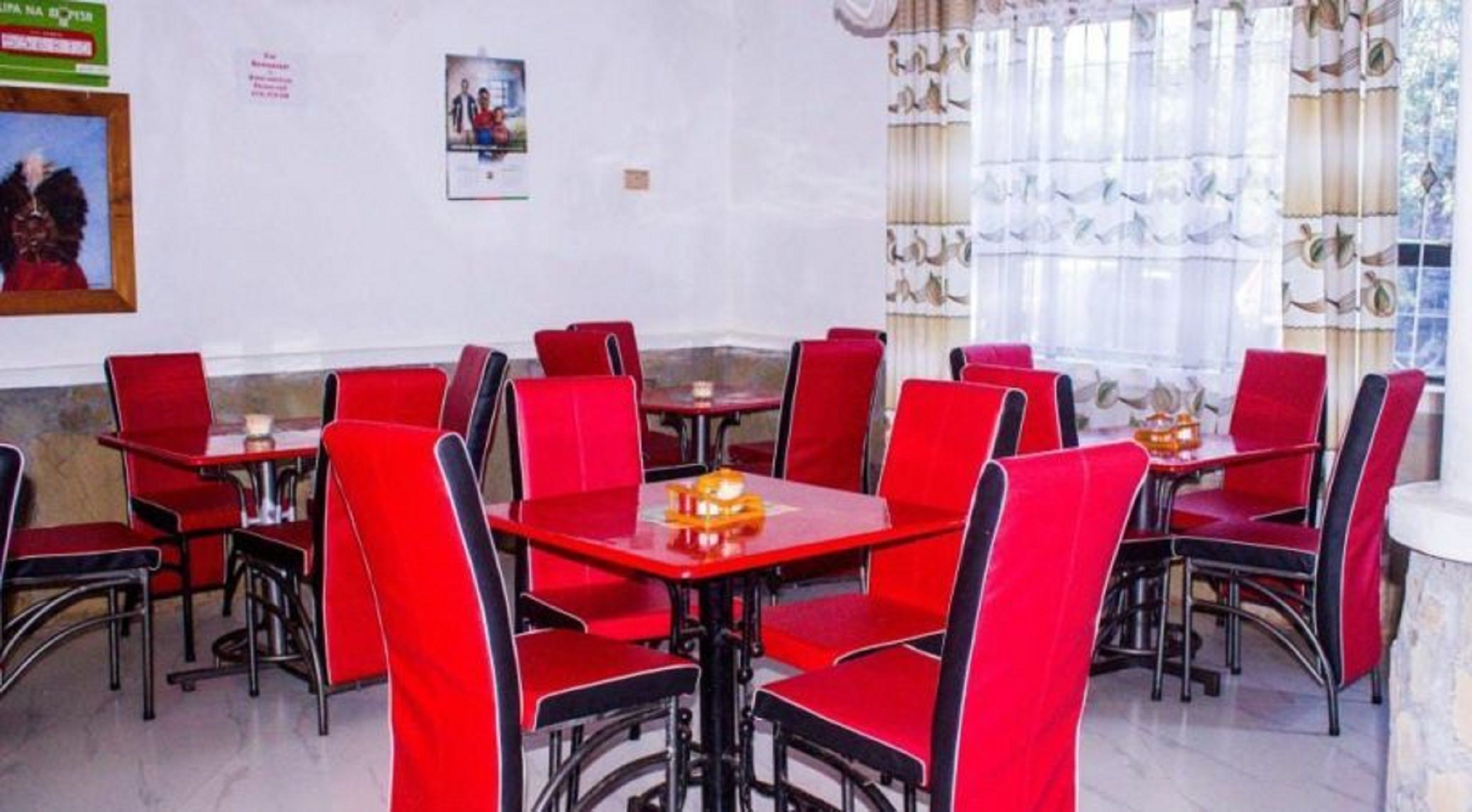 A restaurant with red chairs and tables, white walls, and a window with curtains.