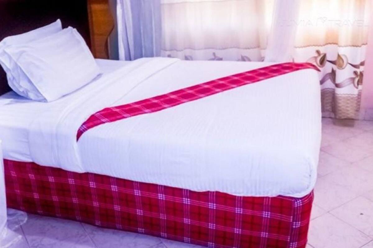 A bed with white bedding and a red plaid bed skirt.