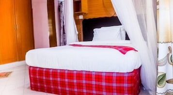 A bed with a white mattress and red plaid skirt, a wooden wardrobe, and a white curtain.